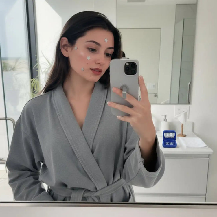 Woman in a gray robe taking a mirror selfie in a bathroom.